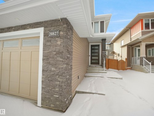 Modern exterior showcasing stacked stone accents, horizontal siding, a beige garage door with transom windows, a dark framed entry door with frosted glass inserts, and a concrete front walkway - 20827 130 Avenue Nw, Edmonton, AB - Outdoor