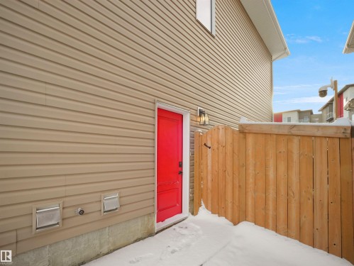 Side entrance featuring a vibrant red door, exterior wall lantern, and a wood privacy fence - 20827 130 Avenue Nw, Edmonton, AB - Outdoor With Exterior