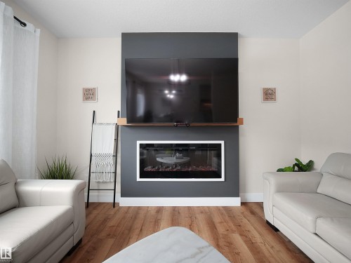 Contemporary fireplace feature wall with a wood-finish mantel and integrated electric fireplace - 20827 130 Avenue Nw, Edmonton, AB - Indoor Photo Showing Living Room With Fireplace