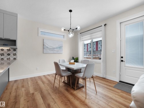 Dining area featuring wood-finish flooring, a modern chandelier with spherical glass shades, and a large window with white blinds - 20827 130 Avenue Nw, Edmonton, AB - Indoor Photo Showing Dining Room