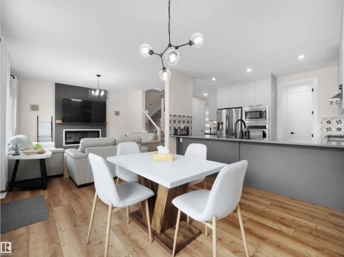 Open-concept living space featuring wood-finish flooring, a modern kitchen with stainless steel appliances and grey cabinetry, a dining area with contemporary lighting, a living room with a built-in fireplace, and a visible staircase - 20827 130 Avenue Nw, Edmonton, AB - Indoor Photo Showing Dining Room