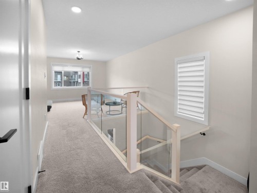 Carpeted upper-level landing featuring a contemporary glass and wood railing system, a recessed lighting fixture, and a window with blinds - 20827 130 Avenue Nw, Edmonton, AB - Indoor Photo Showing Other Room