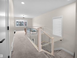 Carpeted upper-level landing featuring a contemporary glass and wood railing system, a recessed lighting fixture, and a window with blinds - 