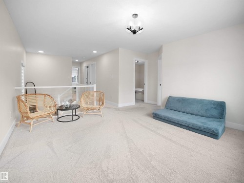 Spacious carpeted room featuring a modern ceiling light fixture, neutral wall paint, white baseboards, and a contemporary glass railing - 20827 130 Avenue Nw, Edmonton, AB - Indoor Photo Showing Other Room