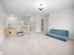 Spacious carpeted room featuring a modern ceiling light fixture, neutral wall paint, white baseboards, and a contemporary glass railing - 