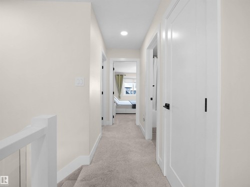 Carpeted hallway featuring white walls, contemporary recessed lighting, white doors with matte black hardware, and a white stair railing with thin balusters - 20827 130 Avenue Nw, Edmonton, AB - Indoor Photo Showing Other Room
