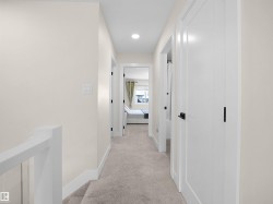 Carpeted hallway featuring white walls, contemporary recessed lighting, white doors with matte black hardware, and a white stair railing with thin balusters - 