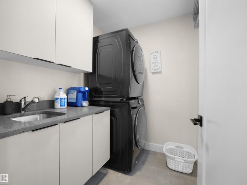 Dedicated laundry area featuring a stacked appliance set, white cabinetry, a countertop with an integrated sink, and tile flooring - 20827 130 Avenue Nw, Edmonton, AB - Indoor Photo Showing Laundry Room