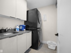 Dedicated laundry area featuring a stacked appliance set, white cabinetry, a countertop with an integrated sink, and tile flooring - 