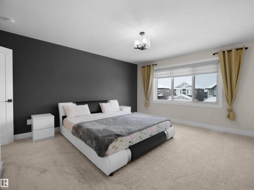 Spacious room featuring a large window, neutral carpeting, a dark accent wall, a solid white door, and a contemporary ceiling fixture - 20827 130 Avenue Nw, Edmonton, AB - Indoor Photo Showing Bedroom