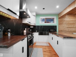 Modern kitchen featuring white cabinetry, wood-finish countertops, and a black marble-effect backsplash - 