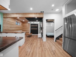 Open-concept space featuring wood-finish flooring, white cabinetry with contrasting countertops, recessed lighting, and a stainless steel refrigerator - 