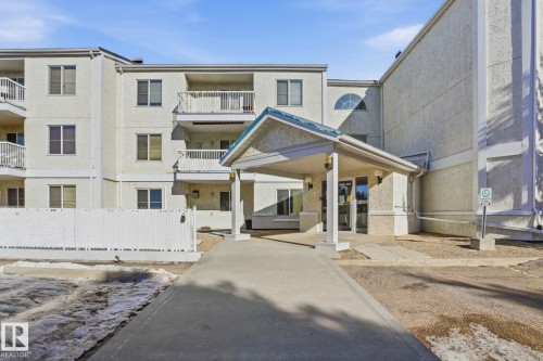 Multi-story building exterior with textured light-colored stucco, multiple balconies with white railings, and a covered entranceway - 309 20 Grange Drive, St. Albert, AB - Outdoor With Balcony With Facade