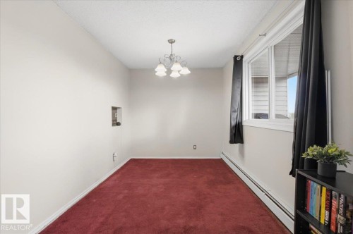 Spacious room featuring red carpeting, a contemporary ceiling light fixture, and a large window with white framing - 6 3803 76 Street, Edmonton, AB - Indoor Photo Showing Other Room