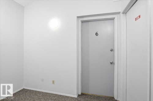 Entry door with number "6" and chrome hardware, accompanied by a flush-mount wall light fixture - 6 3803 76 Street, Edmonton, AB - Indoor Photo Showing Other Room