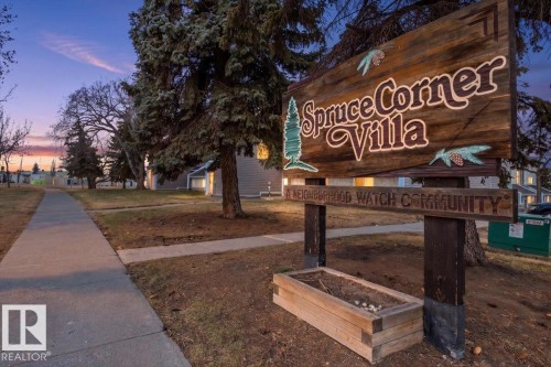 Community entrance sign crafted from wood, featuring "Spruce Corner Villa" text and decorative pinecone accents - 6 3803 76 Street, Edmonton, AB - Outdoor
