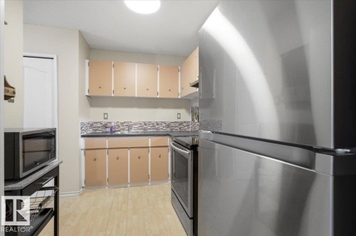 Kitchen featuring wood-finish flooring, light-toned cabinetry, dark countertops, and a mosaic tile backsplash - 6 3803 76 Street, Edmonton, AB - Indoor Photo Showing Kitchen