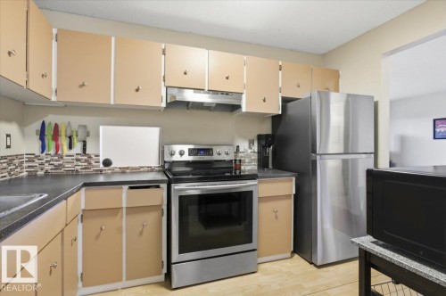 Kitchen featuring a stainless steel range, stainless steel refrigerator, dark countertops, a tiled backsplash, and light-toned cabinetry - 6 3803 76 Street, Edmonton, AB - Indoor Photo Showing Kitchen