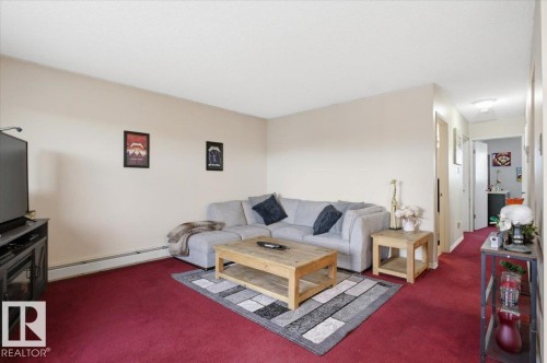 Spacious living area featuring neutral wall paint, red carpeting, and white baseboard heating - 6 3803 76 Street, Edmonton, AB - Indoor Photo Showing Living Room