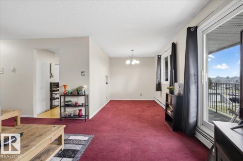 Living area featuring red carpet flooring, light-toned walls, and a sliding glass door providing access to an exterior balcony - 6 3803 76 Street, Edmonton, AB - Indoor