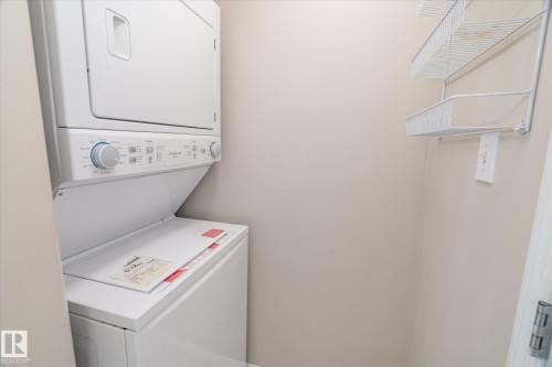 Dedicated laundry area featuring a stacked washer and dryer unit, and wall-mounted wire shelving - 203 155 Edwards Drive, Edmonton, AB - Indoor Photo Showing Laundry Room