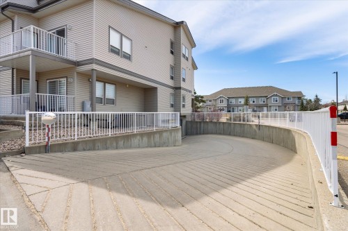 Curved concrete ramp access to underground parking, featuring a white metal railing and a convex safety mirror - 203 155 Edwards Drive, Edmonton, AB - Outdoor With Balcony