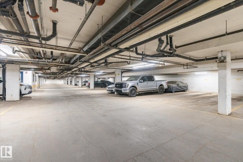 Expansive underground parking garage featuring concrete flooring, structural columns, and overhead lighting - 203 155 Edwards Drive, Edmonton, AB - Indoor Photo Showing Garage