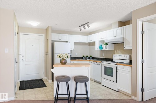 Kitchen featuring white cabinetry, contrasting dark countertops, a white appliance package, and an eat-at island with a butcher block top - 203 155 Edwards Drive, Edmonton, AB - Indoor Photo Showing Kitchen