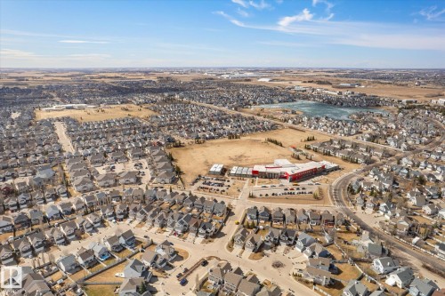 Aerial perspective showcasing a residential development featuring numerous single-family homes, a contemporary red-roofed building, and a large body of water - 203 155 Edwards Drive, Edmonton, AB - Outdoor With View