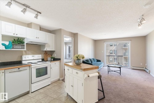 Kitchen featuring white cabinetry, dark countertops, white electric range, and a white dishwasher - 203 155 Edwards Drive, Edmonton, AB - Indoor Photo Showing Kitchen