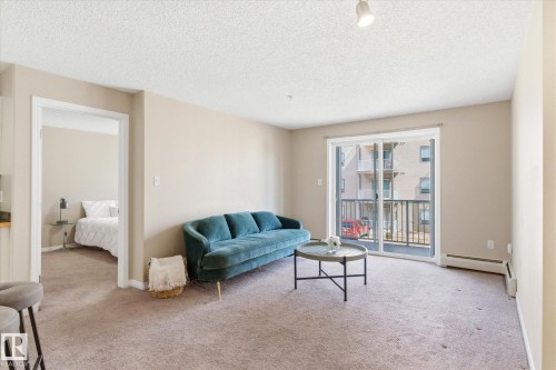 Living area featuring neutral wall tones, carpet flooring, a sliding glass door to a private balcony, track lighting, and white trim - 203 155 Edwards Drive, Edmonton, AB - Indoor Photo Showing Living Room