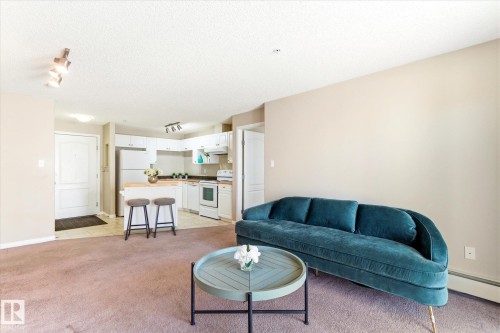 Open-concept living area featuring light neutral wall paint, track lighting, and soft carpet flooring - 203 155 Edwards Drive, Edmonton, AB - Indoor Photo Showing Living Room