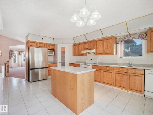 Kitchen featuring light wood cabinetry, white tile flooring, a central island with a solid surface countertop, stainless steel refrigerator, and integrated white appliances - 1054 Ormsby Crescent, Edmonton, AB - Indoor Photo Showing Kitchen