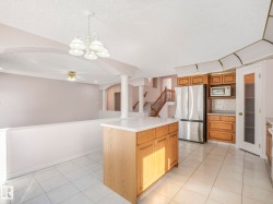 Kitchen featuring a central island with a light-toned countertop, wood-finish cabinetry, stainless steel appliances, and white tile flooring - 
