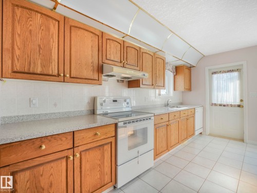 Kitchen featuring wood cabinetry, white tiled flooring, a white tile backsplash, light-colored countertops, and a white freestanding range - 1054 Ormsby Crescent, Edmonton, AB - Indoor Photo Showing Kitchen