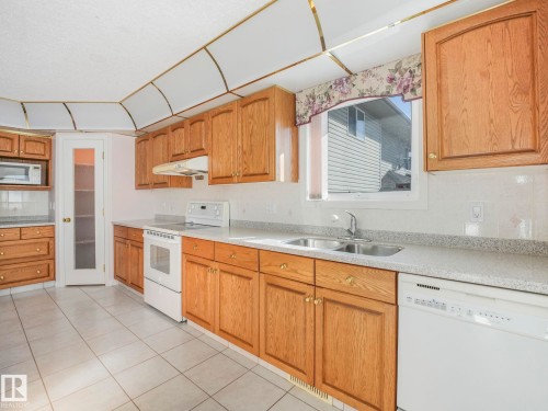 Kitchen featuring wood cabinetry, white tile flooring, laminate countertops, a double basin sink, and a white appliance package including a dishwasher and range - 1054 Ormsby Crescent, Edmonton, AB - Indoor Photo Showing Kitchen With Double Sink