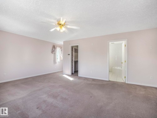 Carpeted interior space featuring a ceiling fan with integrated lighting, a window with drapery, an open closet with shelving, and an open doorway leading to a tiled bathroom with a bathtub - 1054 Ormsby Crescent, Edmonton, AB - Indoor Photo Showing Other Room
