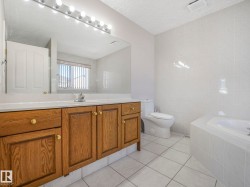 Bathroom featuring a wood-finish vanity with an integrated sink, a large mirror, and wall-mounted vanity lighting - 