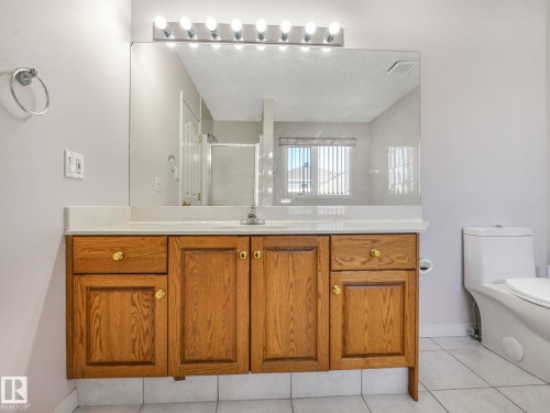 Bathroom vanity featuring wood-finish cabinetry with brass hardware, a light-toned countertop, a large wall-mounted mirror, and a vanity light fixture with multiple bulbs - 1054 Ormsby Crescent, Edmonton, AB - Indoor Photo Showing Bathroom