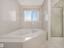Spacious bathroom featuring a built-in jetted tub, ceramic tile surround, and an adjacent glass-enclosed shower - 