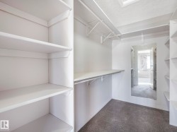 Walk-in wardrobe featuring extensive built-in shelving, hanging rods, and a full-length mirror - 