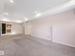 Spacious carpeted room featuring recessed lighting, light gray wall paint, white trim, and a door leading to a kitchen with wood cabinetry and stainless steel appliances - 