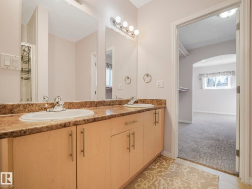 Bathroom vanity featuring dual sinks with individual chrome faucets, a patterned countertop, and light wood-finish cabinetry with brushed nickel pulls - 1054 Ormsby Crescent, Edmonton, AB - Indoor Photo Showing Bathroom