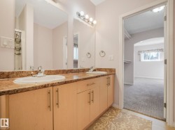 Bathroom vanity featuring dual sinks with individual chrome faucets, a patterned countertop, and light wood-finish cabinetry with brushed nickel pulls - 