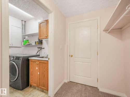 Dedicated laundry area with a utility sink, wood-finish cabinetry, and overhead shelving - 1054 Ormsby Crescent, Edmonton, AB - Indoor Photo Showing Laundry Room