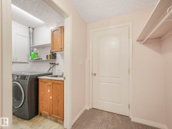 Dedicated laundry area with a utility sink, wood-finish cabinetry, and overhead shelving - 