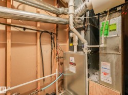 Utility area featuring a forced-air furnace unit, associated ductwork, and exposed plumbing lines - 