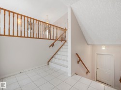 Entry foyer with light-toned tile flooring and a wood railing staircase - 