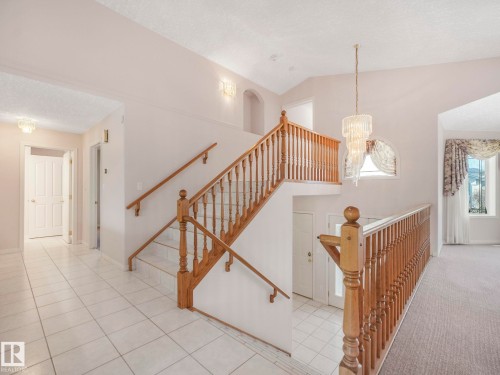 Multi-level interior featuring a grand staircase with wood banisters, decorative chandelier, and arch window - 1054 Ormsby Crescent, Edmonton, AB - Indoor Photo Showing Other Room