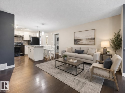 Open-concept living space featuring wood-finish flooring, a kitchen island with seating, pendant lighting, white cabinetry, and a stacked washer and dryer unit - 45 4470 Prowse Road, Edmonton, AB - Indoor Photo Showing Living Room